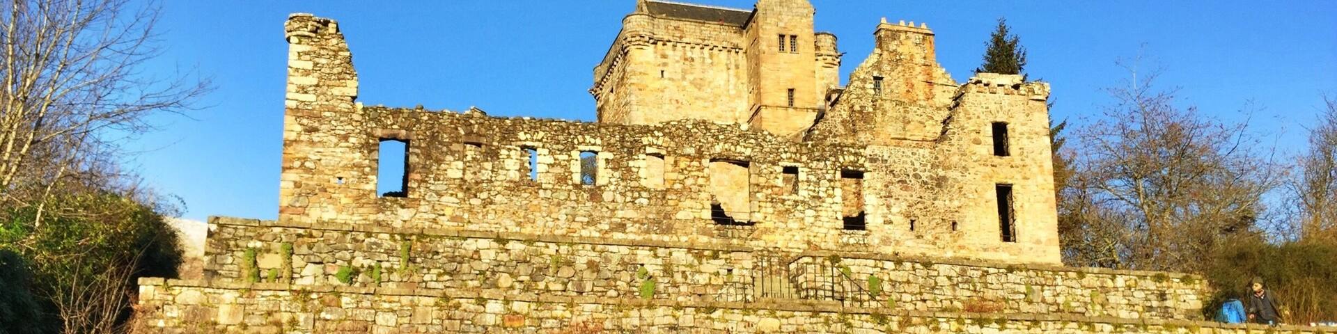 A historic stone castle with a grassy foreground and clear blue sky.