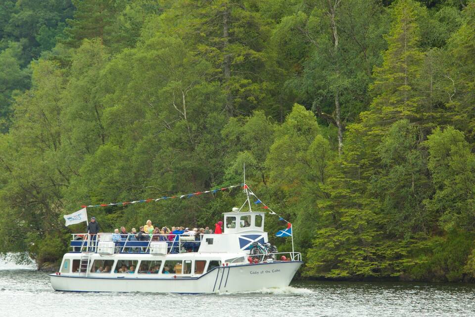 A boat named "Lady of the Lakes" on a river surrounded by dense green forest.