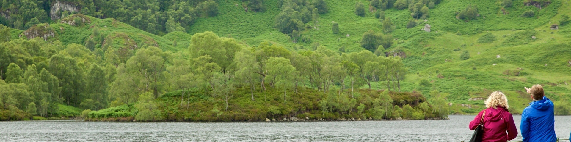 Loch Katrine featuring a lake or waterhole and forests as well as a small group of people