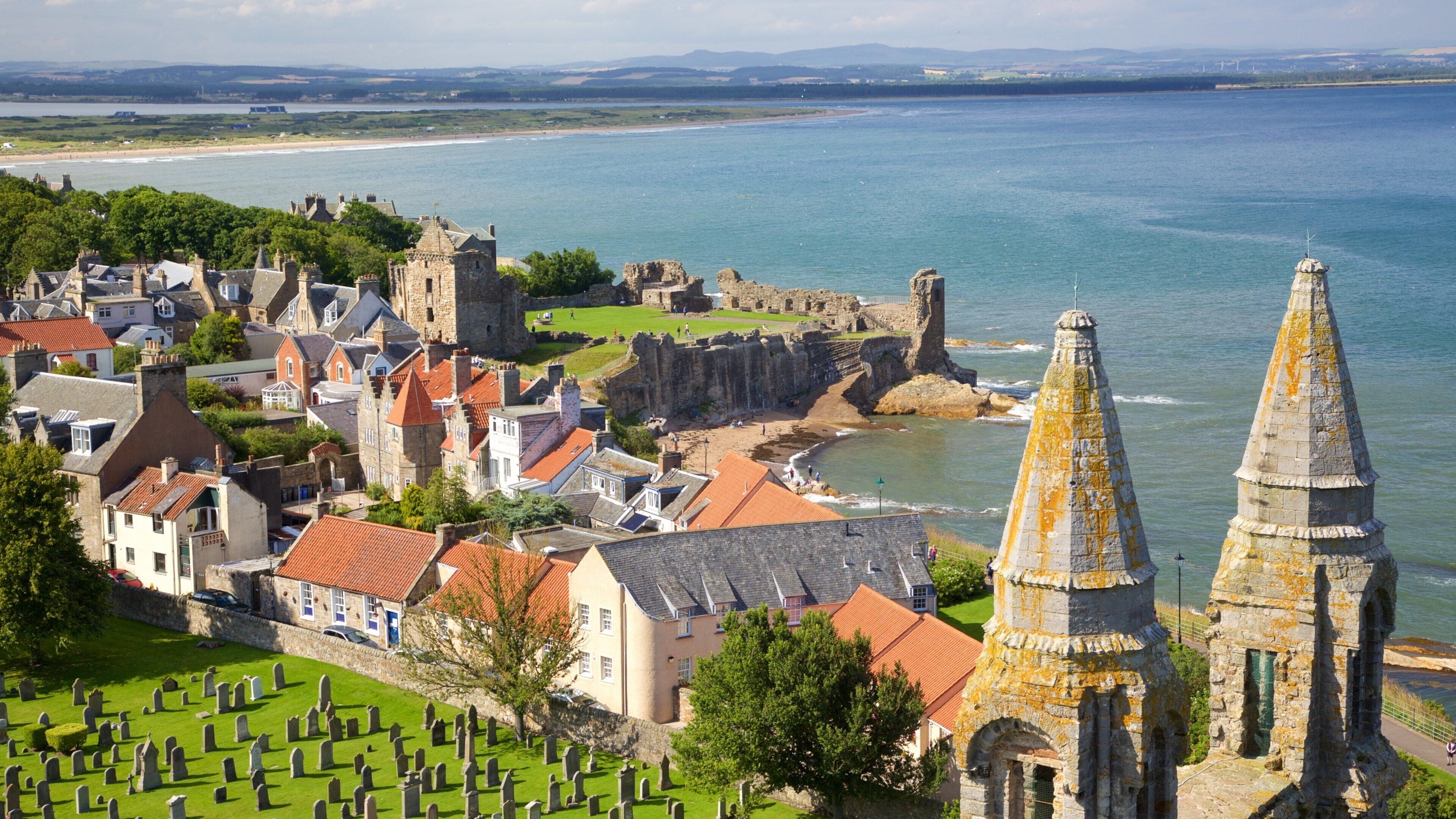 A coastal town with historic buildings, a church spire, and a castle overlooking the sea.