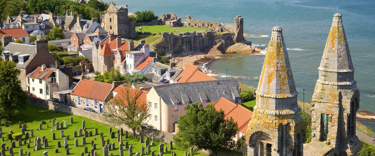 A coastal town with historic buildings, a church spire, and a castle overlooking the sea.