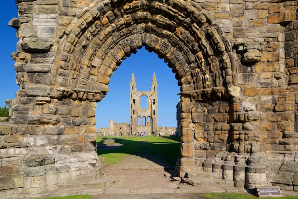 Un arco de piedra antigua que conduce a un edificio histórico con una torre alta.