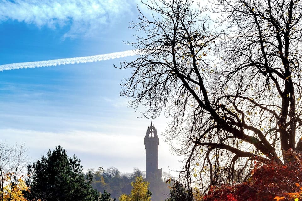 A tower in the distance, surrounded by autumn-colored trees and a grassy field.