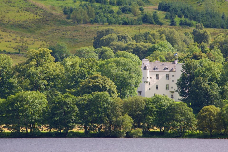 A castle surrounded by dense green trees and hills.