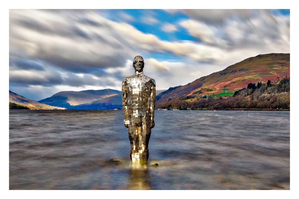 A mosaic statue in a body of water with mountains in the background.