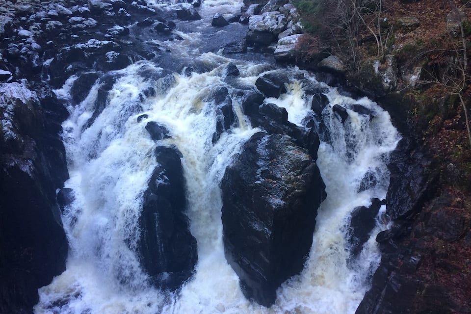 A powerful waterfall cascading over large rocks in a forested area.