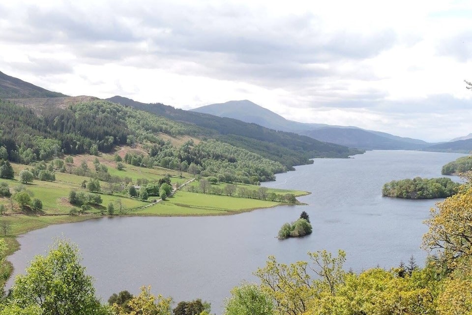 Um lago rodeado por colinas verdes e árvores.