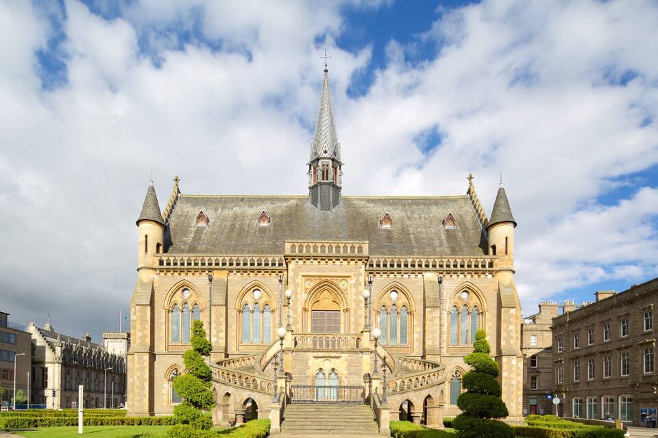 Un bâtiment historique doté d’une haute flèche, de fenêtres en arc et d’une entrée centrale.