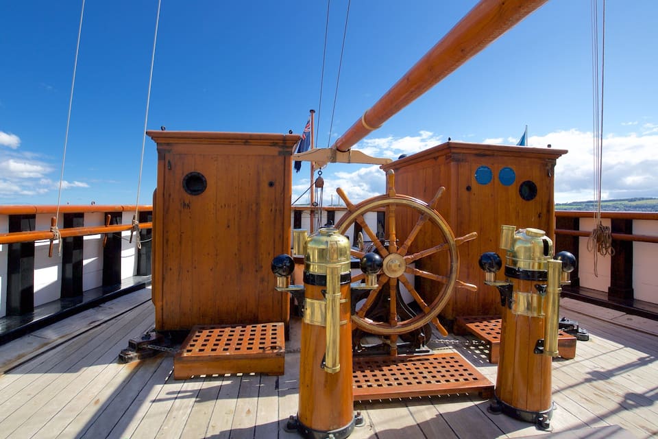 A wooden ship wheel and brass instruments on a deck with a clear sky.