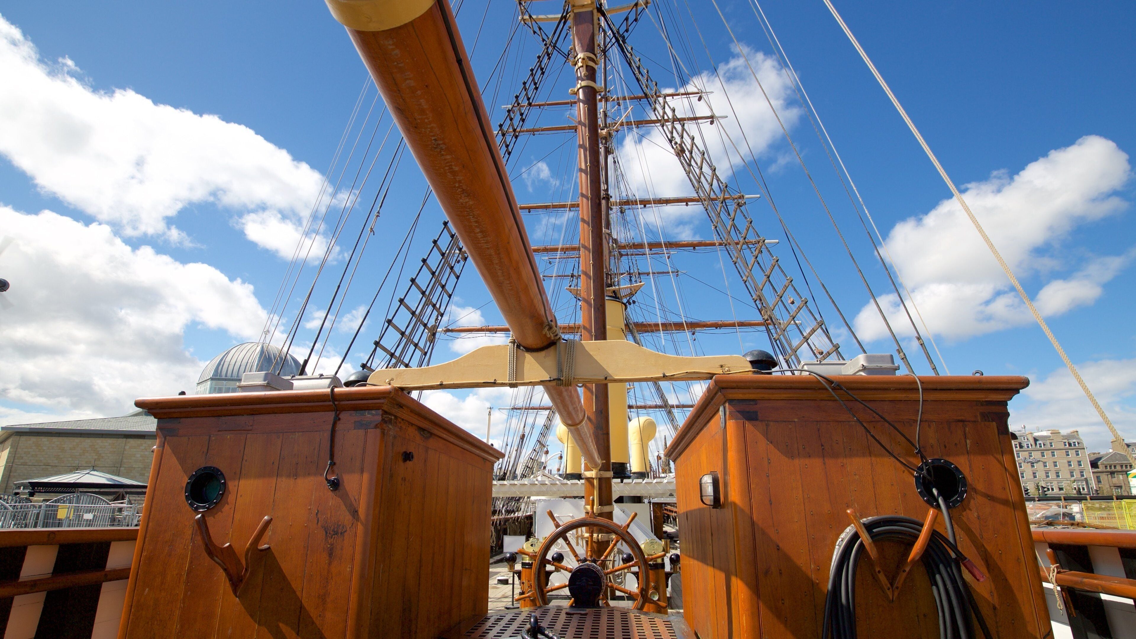 A ship's deck with a large wooden wheel, masts, and rigging.