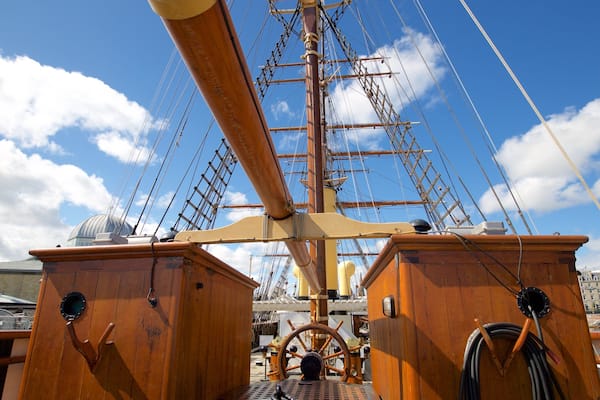 A ship's deck with a large wooden wheel, masts, and rigging.