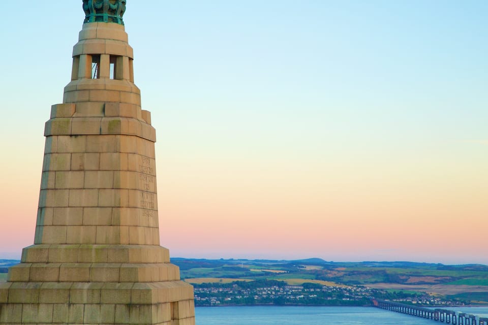 Um monumento de pedra com inscrições, com vista para um rio e uma cidade distante.