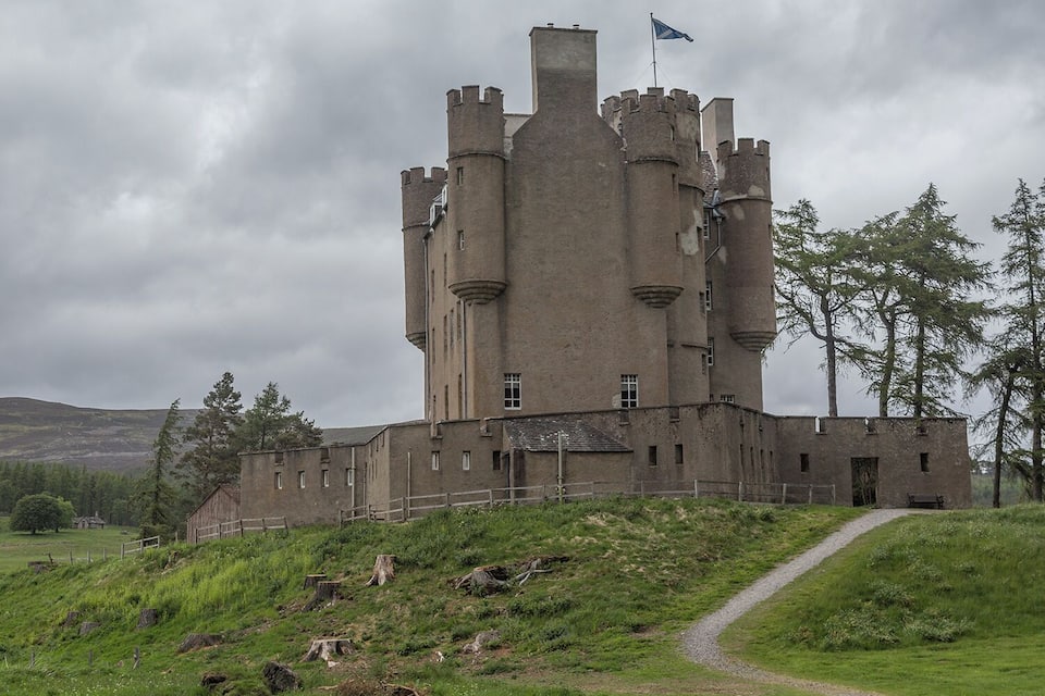 A castle with multiple towers, a flag, and a surrounding landscape with trees and a hill.