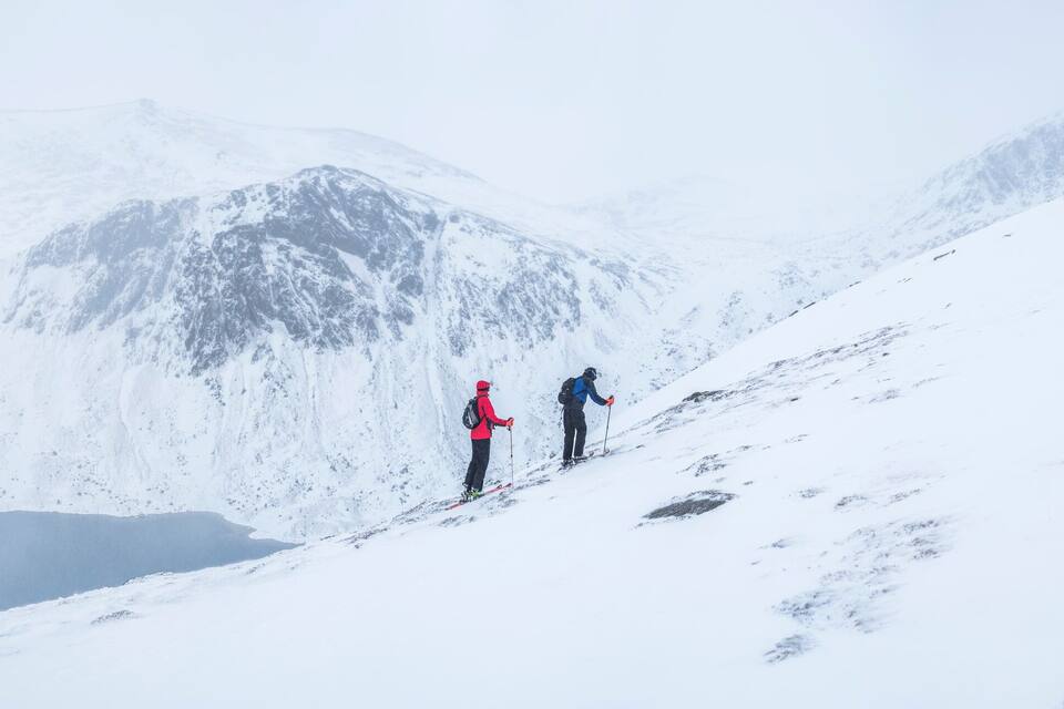 A snowy mountain landscape with two skiers descending a slope.