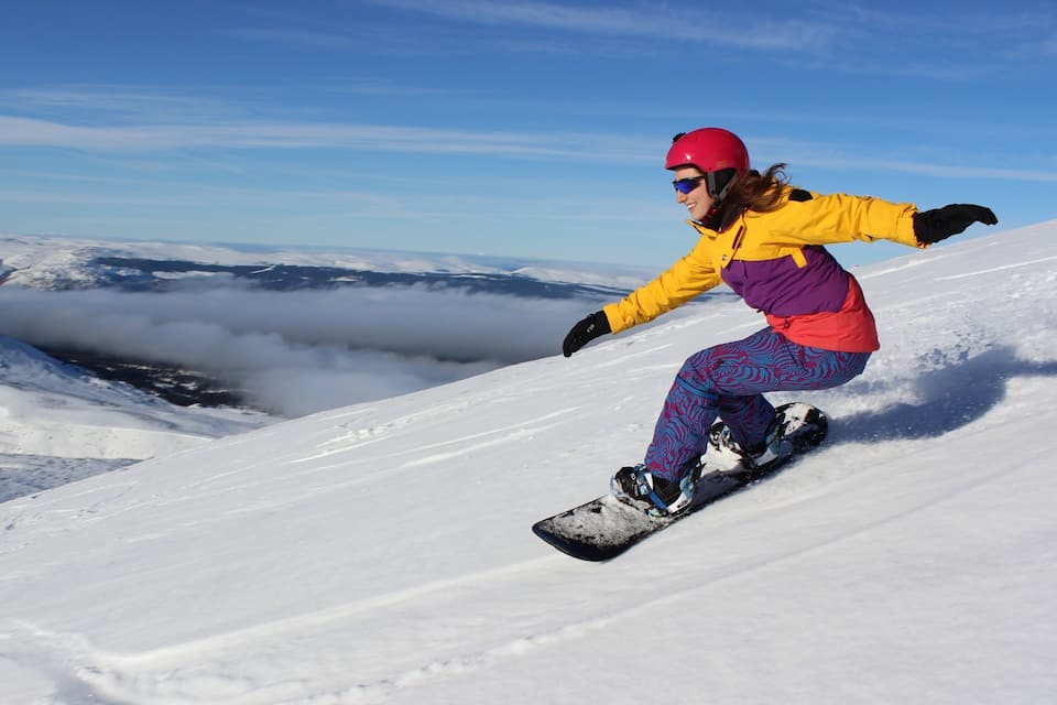 A snowboarder on a snowy mountain slope with clouds below.