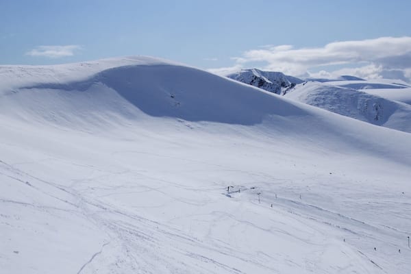 A snow-covered mountain landscape with undulating terrain and distant peaks.