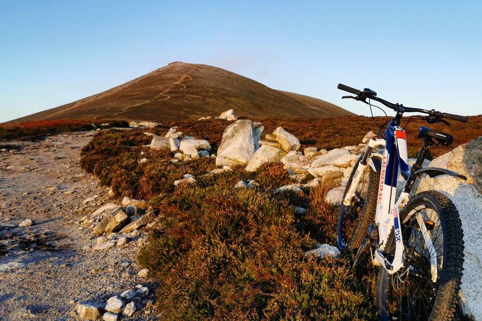 Een berg met heldere lucht, rotsachtig terrein en een mountainbike aan de kant geparkeerd.