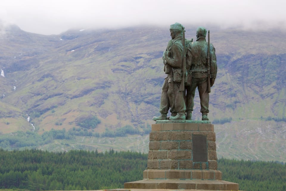 Une statue représentant deux soldats, placée sur un piédestal, avec un paysage montagneux en arrière-plan.