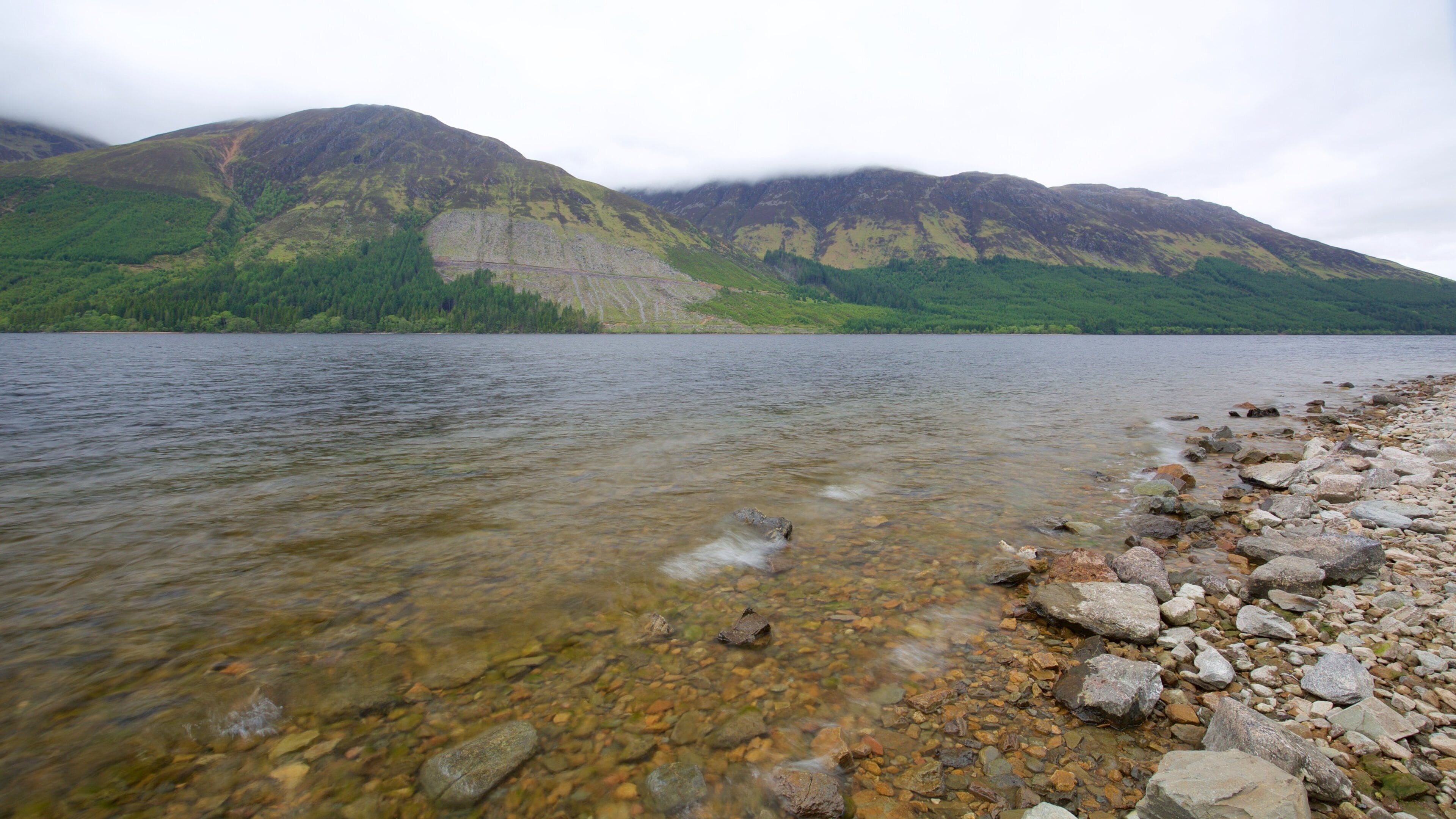 A clear lake with a rocky shoreline and mountains in the background.