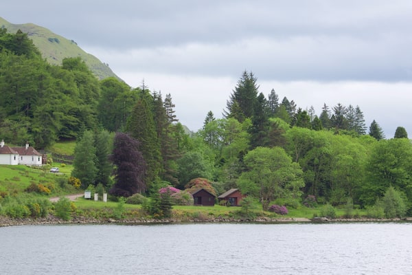 Un lac bordé de maisons, entouré de collines verdoyantes et d’arbres.
