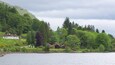 A lake with houses on the shore, surrounded by lush green hills and trees.