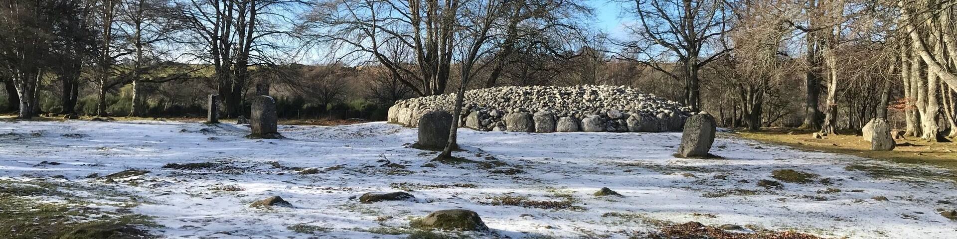 A snowy landscape with stone circles and leafless trees.