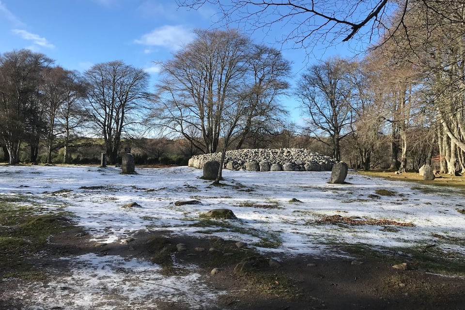 A snowy landscape with stone circles and leafless trees.