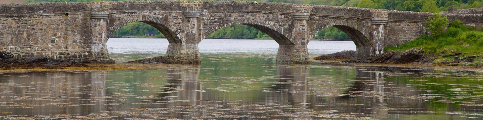 A stone bridge over a body of water with hills in the background.