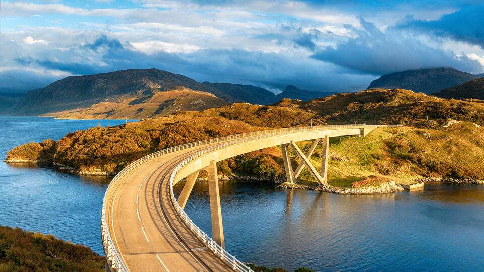 A bridge over a body of water with mountains in the background.