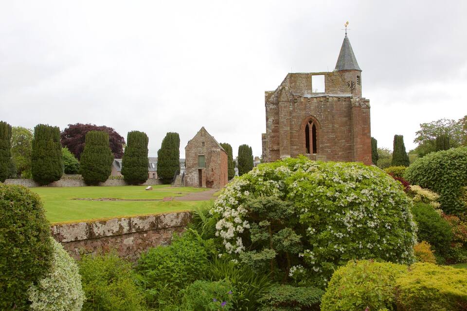 Eine historische Kirche mit einem hohen Turm und Wetterfahne, umgeben von gepflegten Gärten und alten Steinbauten.