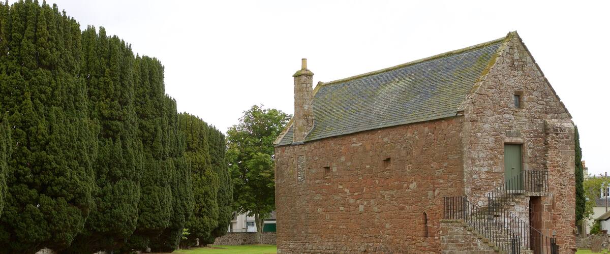 A stone building with a tiled roof, surrounded by a well-maintained lawn and tall trees.