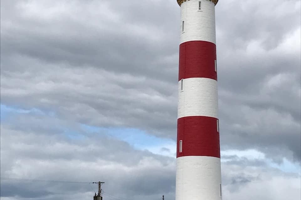 A tall lighthouse with alternating red and white stripes, a small adjacent building, and a cloudy sky.