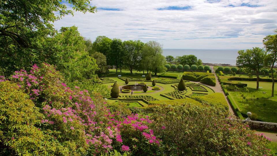 A formal garden with geometrically shaped hedges, a central fountain, and a view of the sea.
