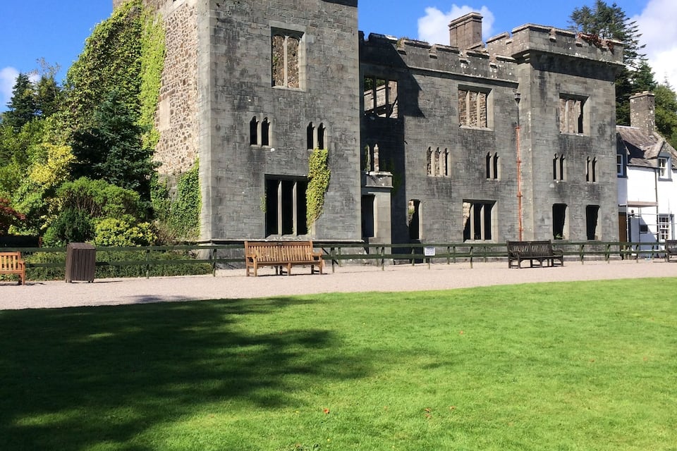 A large stone castle with ivy-covered walls, a grassy courtyard, and wooden benches.