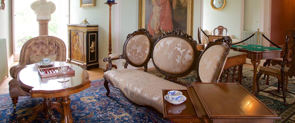 A room with antique furniture, including a sofa, chairs, a table, and a billiards table. There is a painting on the wall, a bust on a pedestal, and a potted plant.