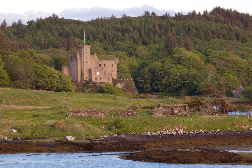 A castle on a hill, surrounded by dense forest and a body of water.