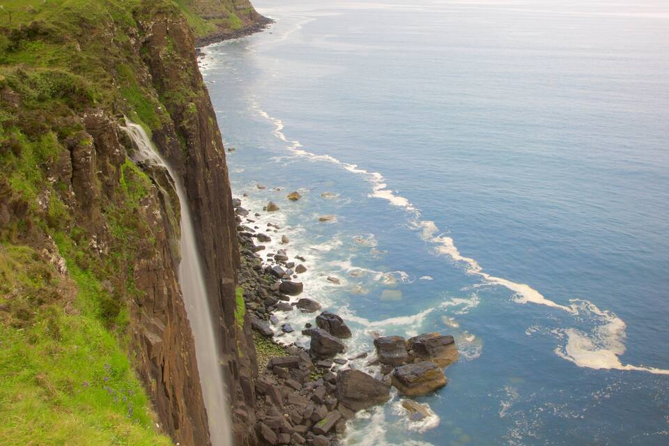 A coastal cliff with a waterfall, rocky shoreline, and ocean waves.