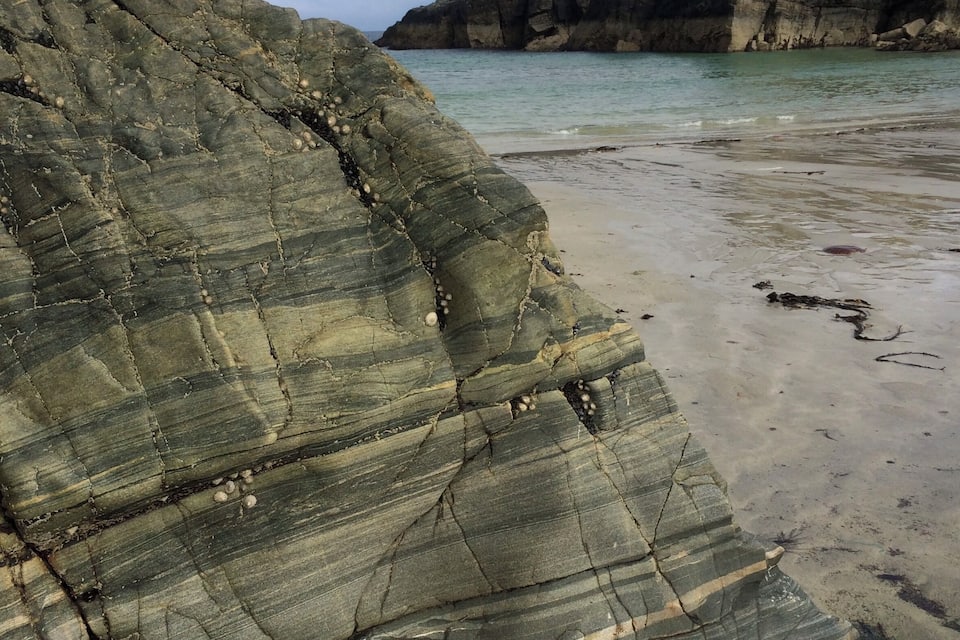 Une côte rocheuse, avec des formations rocheuses à stratification visible et une plage de sable.