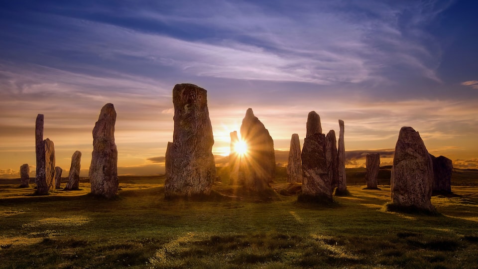 Stonehenge standing in a grassy field with the sun setting behind the stones.