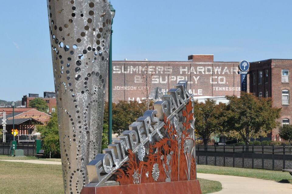 A metal sculpture with holes, a sign for Sumner's Hardware Supply Co., and a brick building in the background.