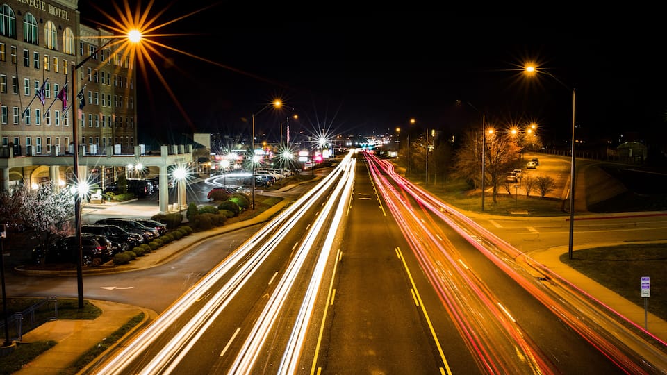 A nighttime city street with light trails from moving vehicles, a prominent building labeled "Carnegie Hotel," and streetlights lining the road.