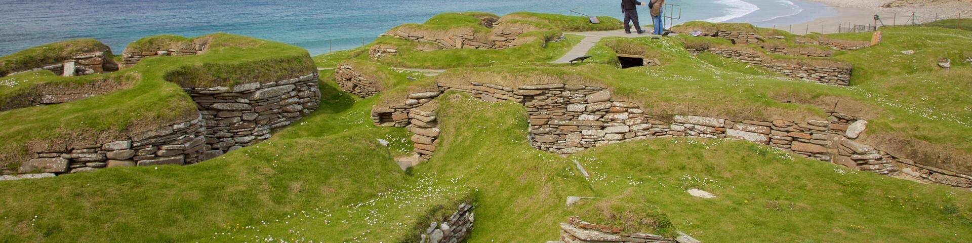 Ancient stone structures on a grassy hillside overlooking a beach.
