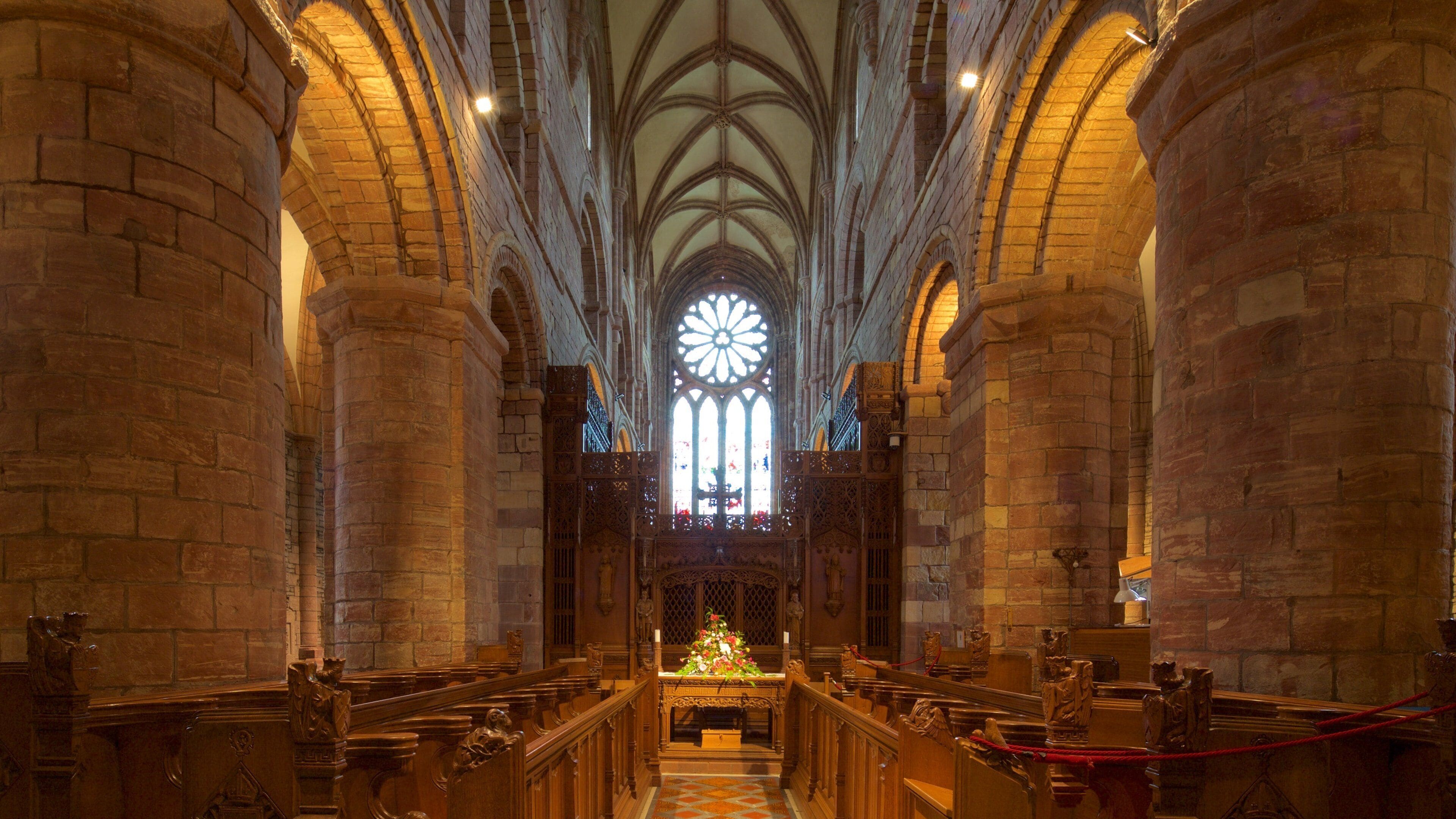 A cathedral interior with high vaulted ceilings, large stained glass windows, and ornate wooden pews.