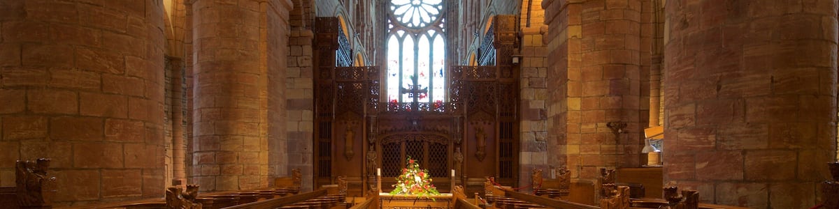 L’intérieur d’une cathédrale, avec de hauts plafonds en voûte, de grandes fenêtres ornées de vitraux et des bancs en bois richement décorés.