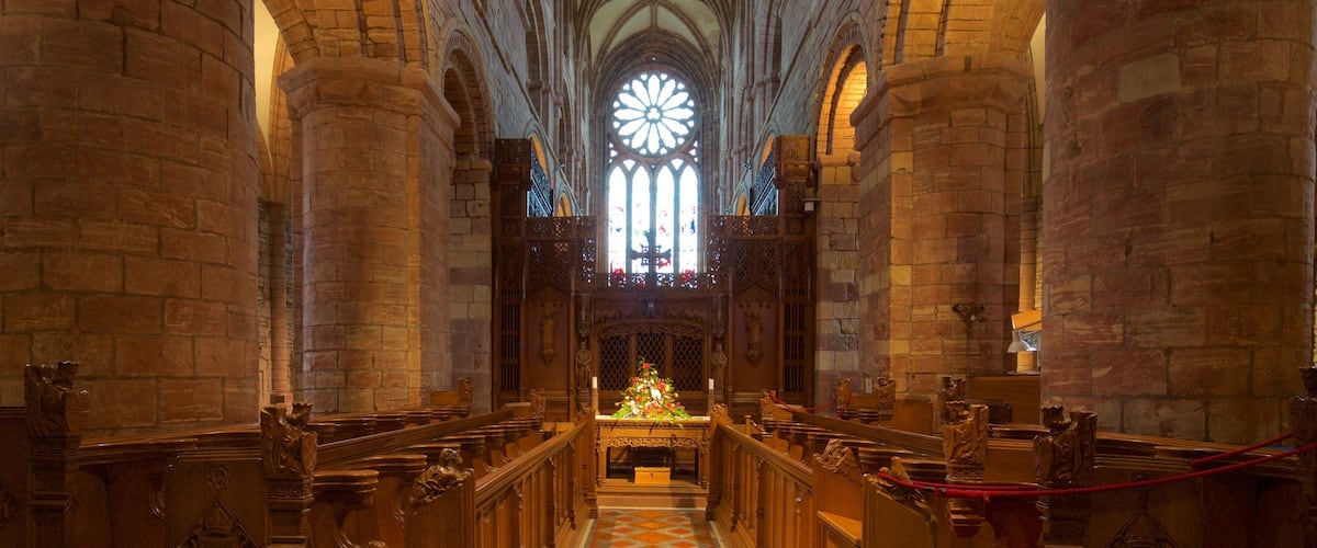 A cathedral interior with high vaulted ceilings, large stained glass windows, and ornate wooden pews.