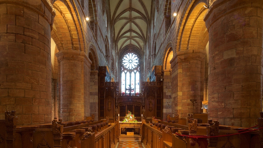 Interior de uma catedral com altos tetos abobadados, grandes janelas de vitrais e bancos de madeira ornamentados.