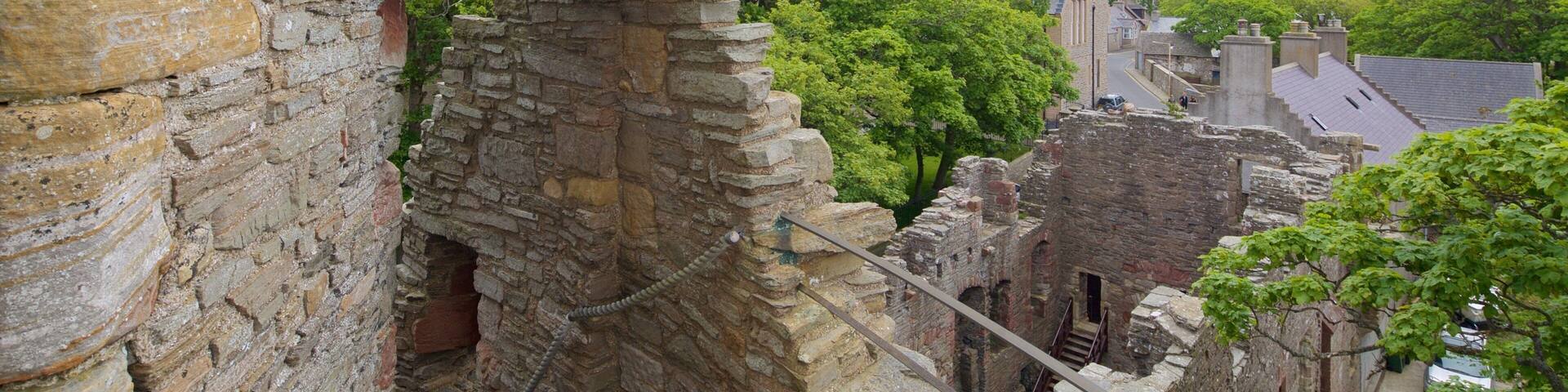 A stone staircase leading to a partially ruined stone building with a view of a town and greenery in the background.