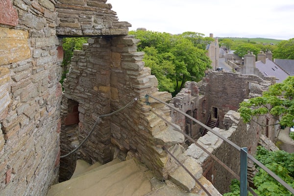 Un escalier en pierre mène à un bâtiment en pierre en partie en ruine, d’où l’on peut admirer une vue sur la ville et la verdure en arrière-plan.