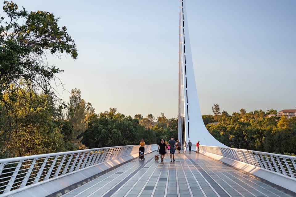 A pedestrian bridge with a white railing and a tall, slender tower.