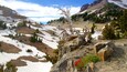 A mountainous landscape with snow patches, a dead tree, and red flowers on rocks.